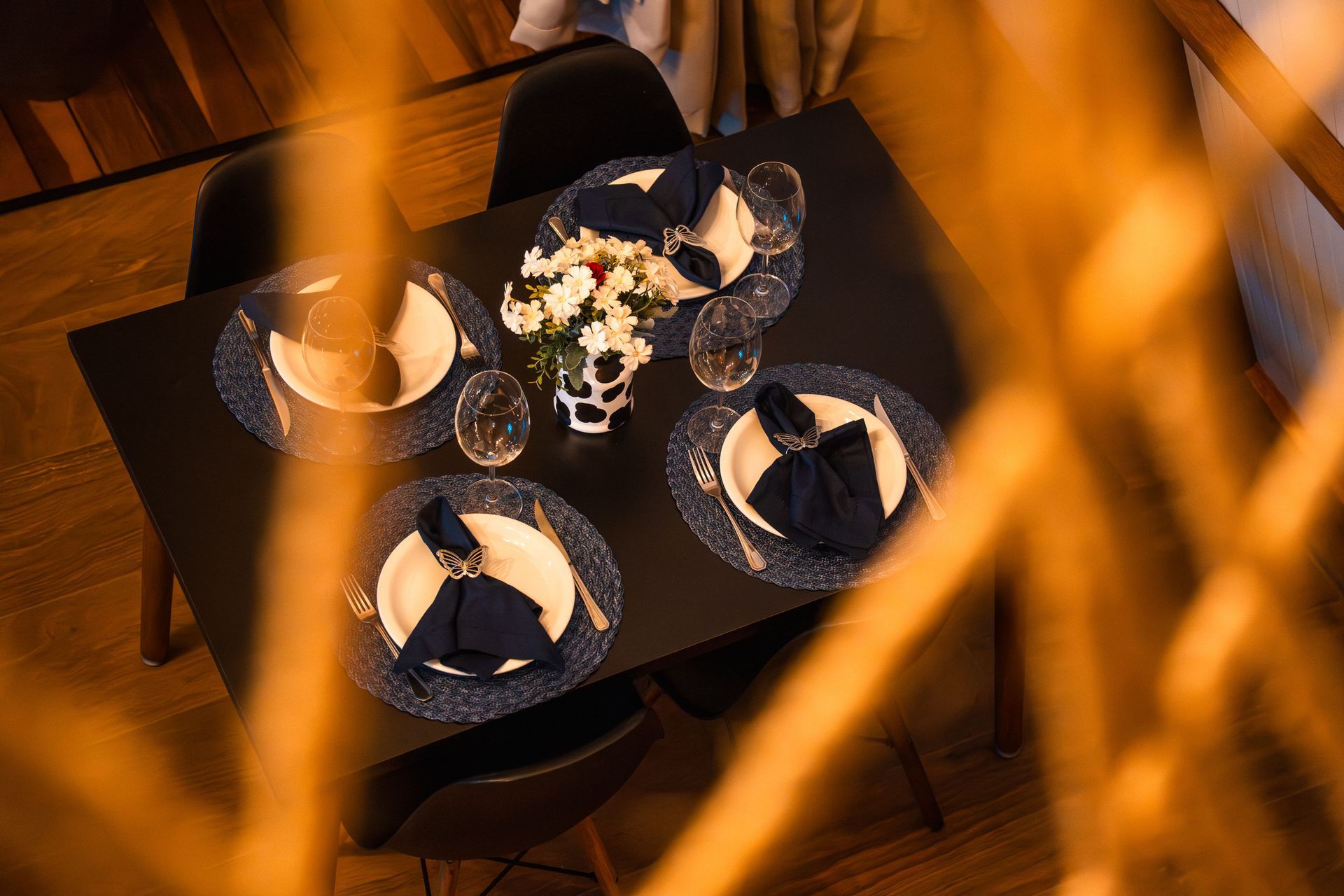 Conjunto de mesa de jantar preto para quatro pessoas, com pratos, guardanapos e flores. Chalé Mont Hermon.