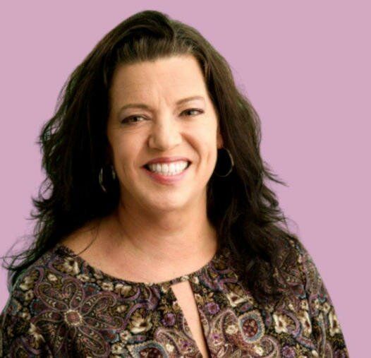 A woman in a paisley shirt is smiling and wearing hoop earrings.