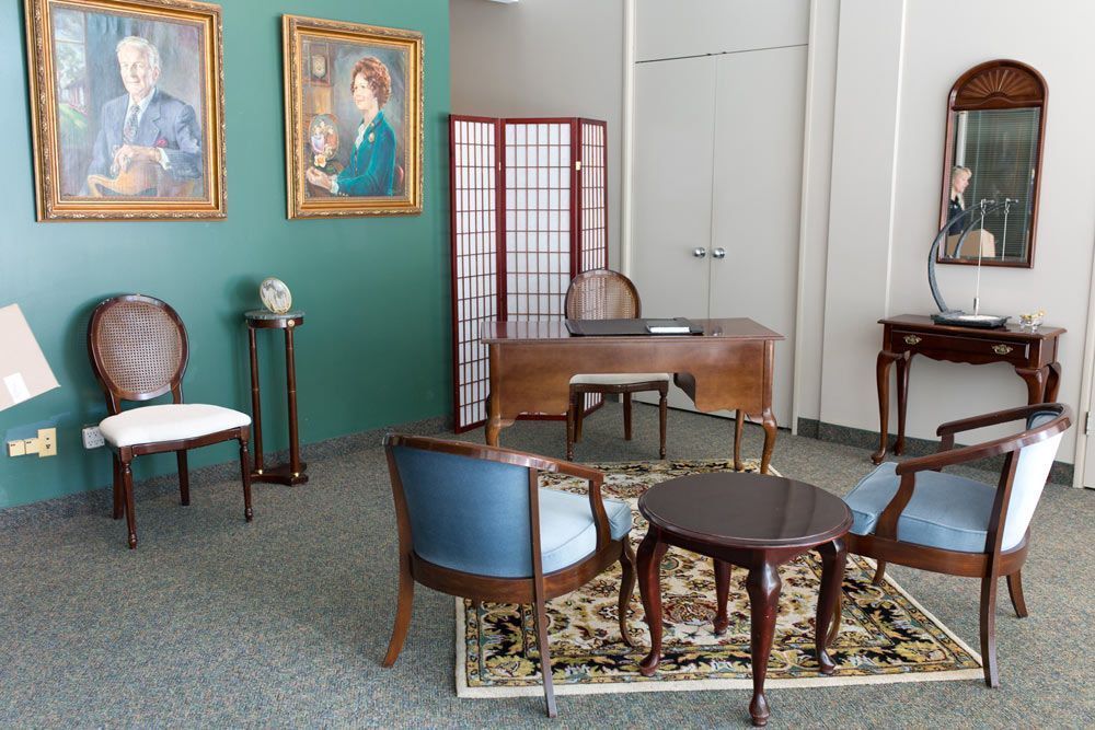 A living room with a desk and chairs and two paintings on the wall