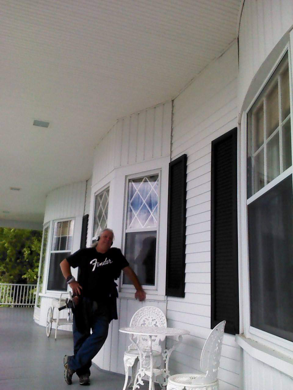 A man standing on a porch wearing a fender shirt