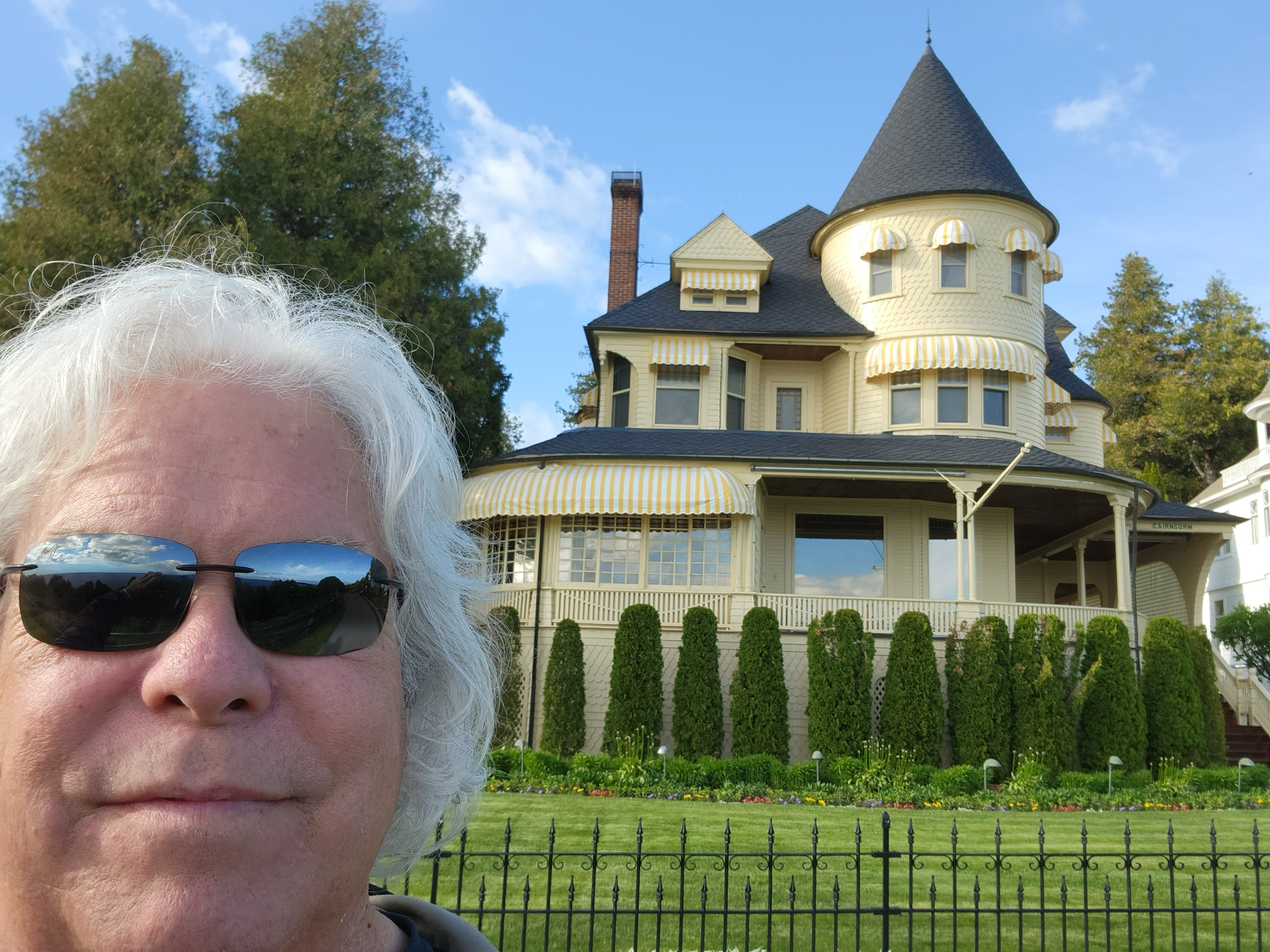 A man wearing sunglasses stands in front of a large house