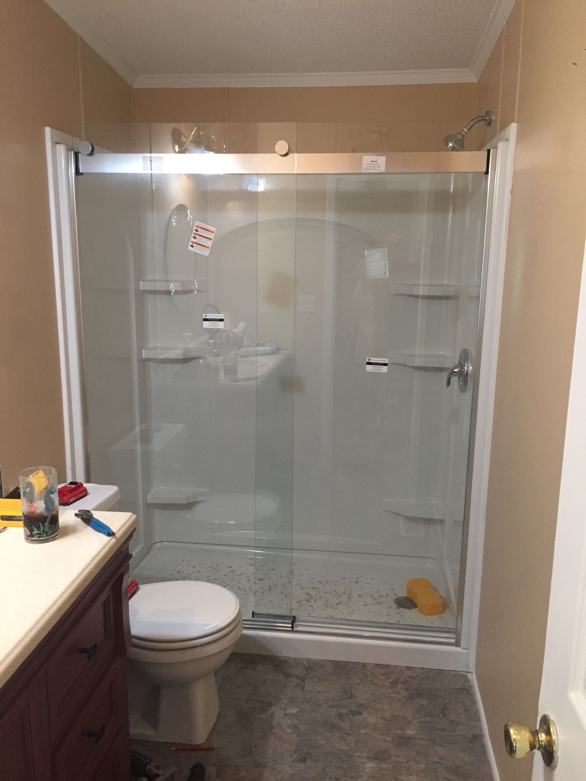 Bathroom with a white shower, toilet, and brown vanity; beige walls and dark floor.