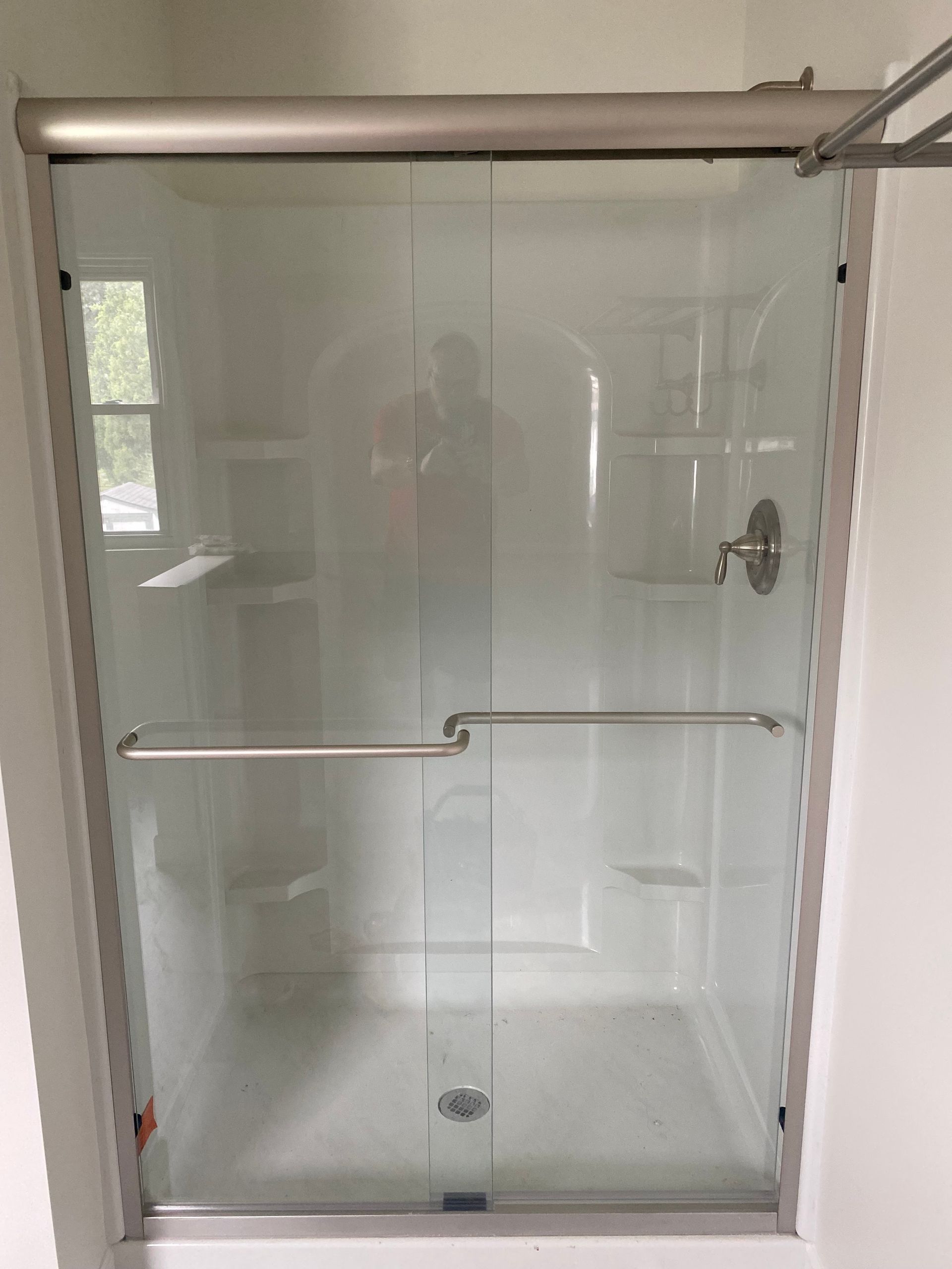 A shower enclosure with a sliding glass door and a silver frame, set in a white-walled bathroom.