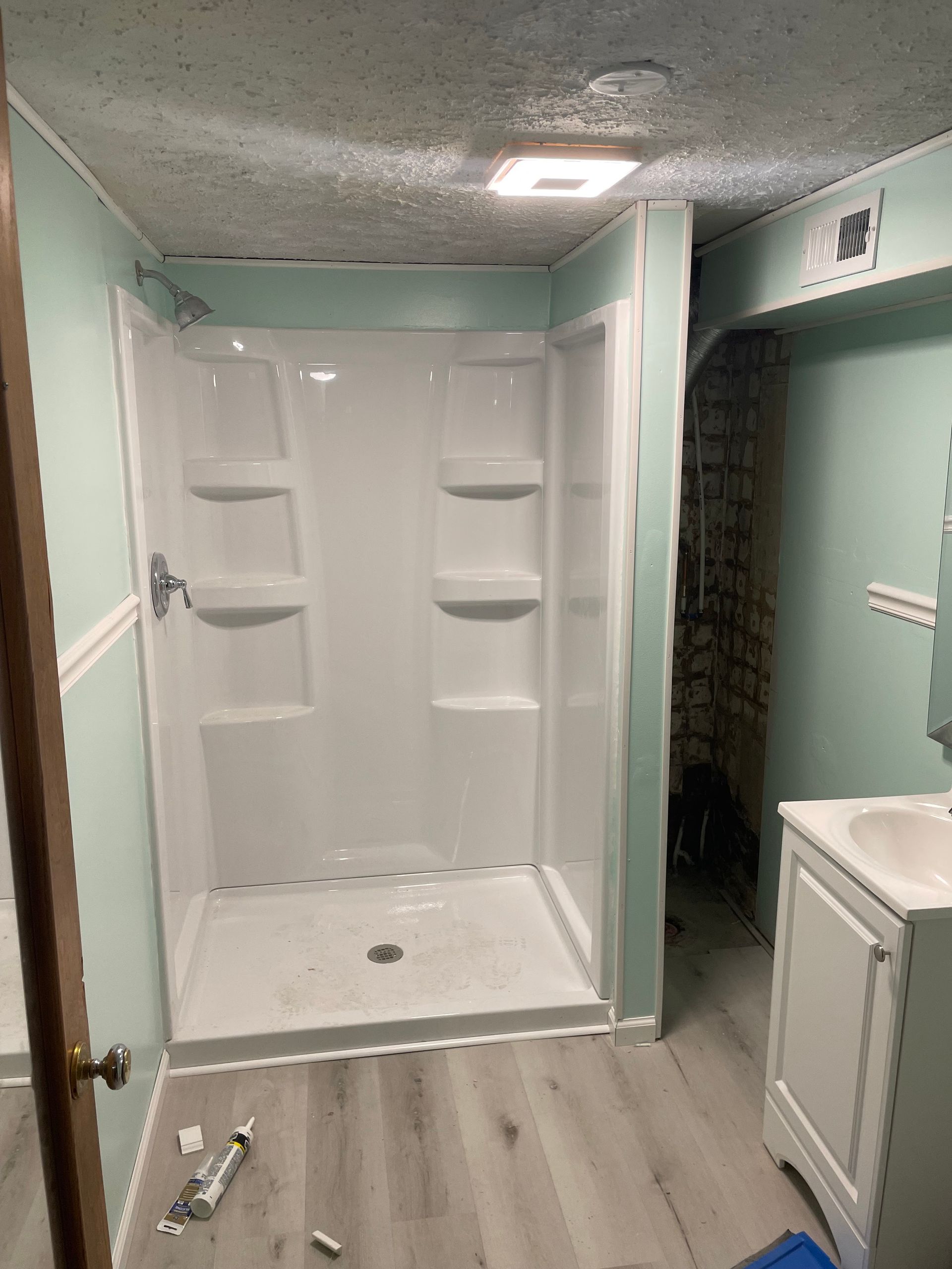 Bathroom with white shower stall, light blue walls, gray wood-look flooring, and white vanity.