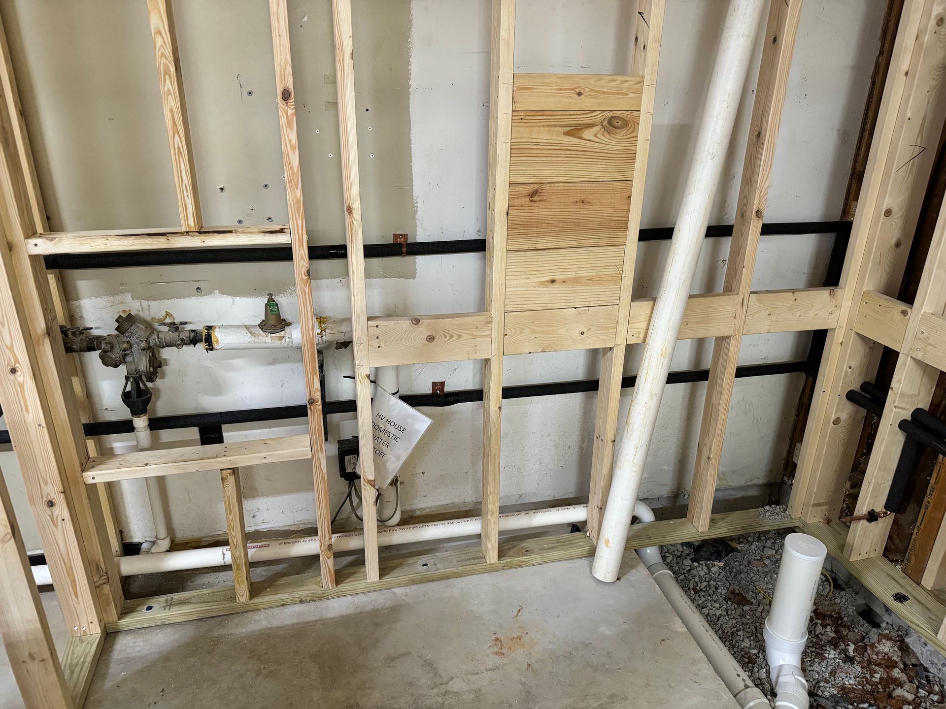 Framed wall construction with exposed pipes. Black and white pipes against wooden beams.