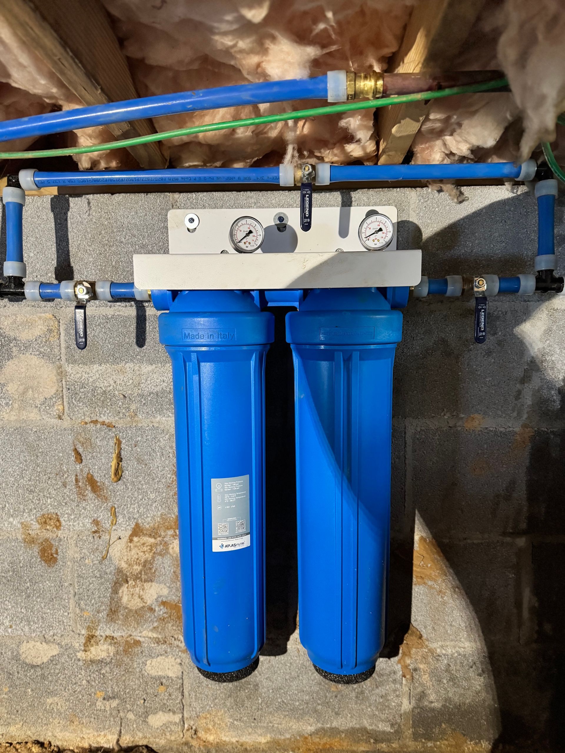 Blue water filter system mounted on a gray concrete wall, with blue and green pipes.