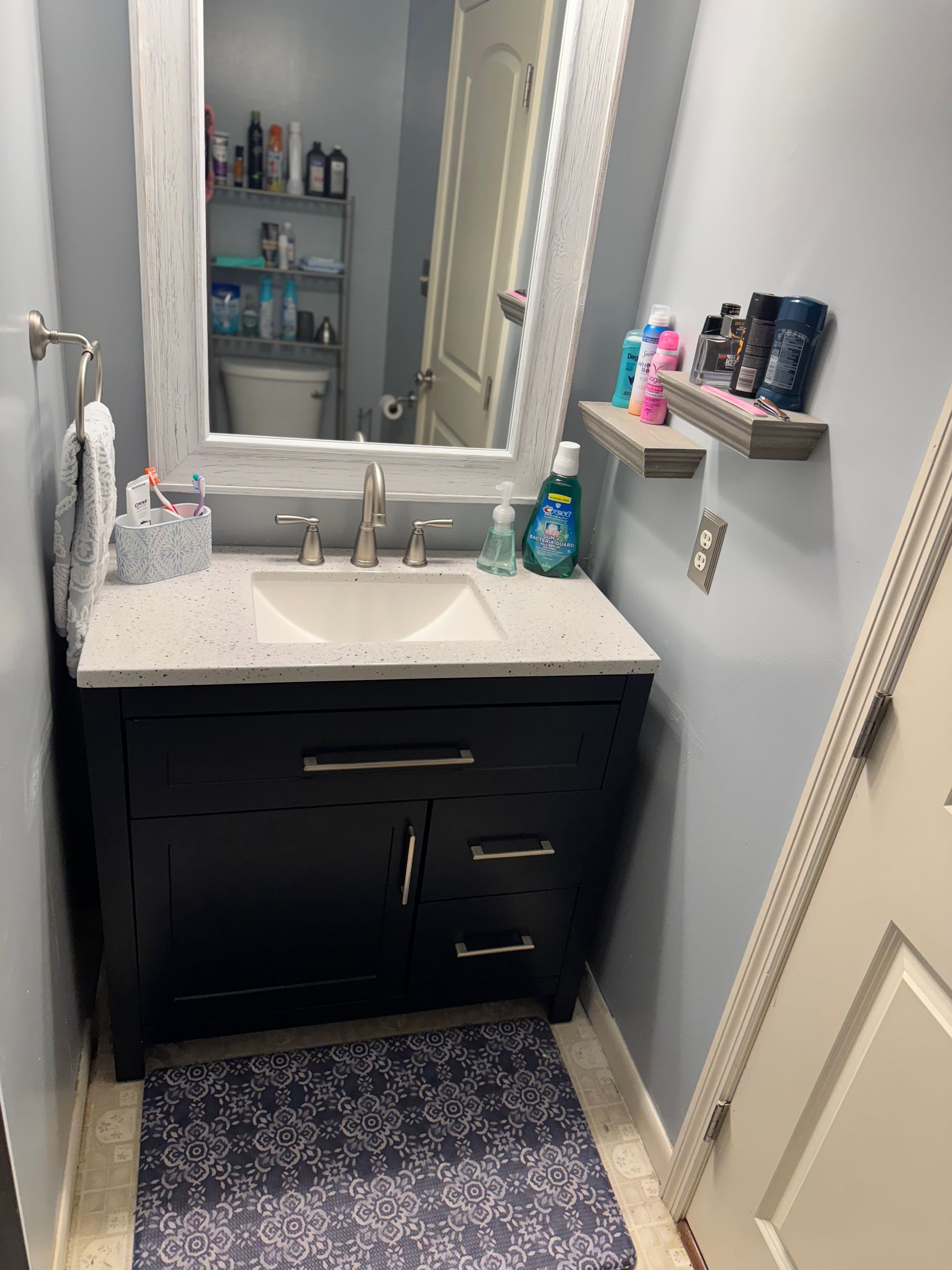 Bathroom with navy vanity, white countertop, silver faucet, and framed mirror. Gray walls, bath mat.