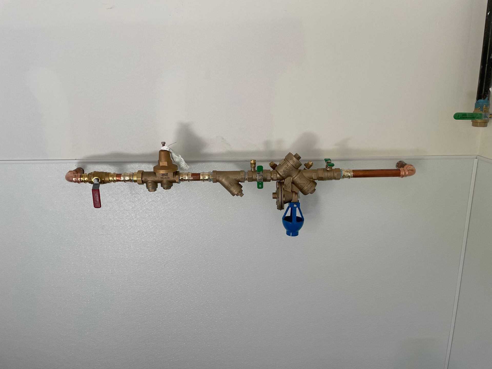 Copper pipes with valves and a pressure regulator mounted on a wall.