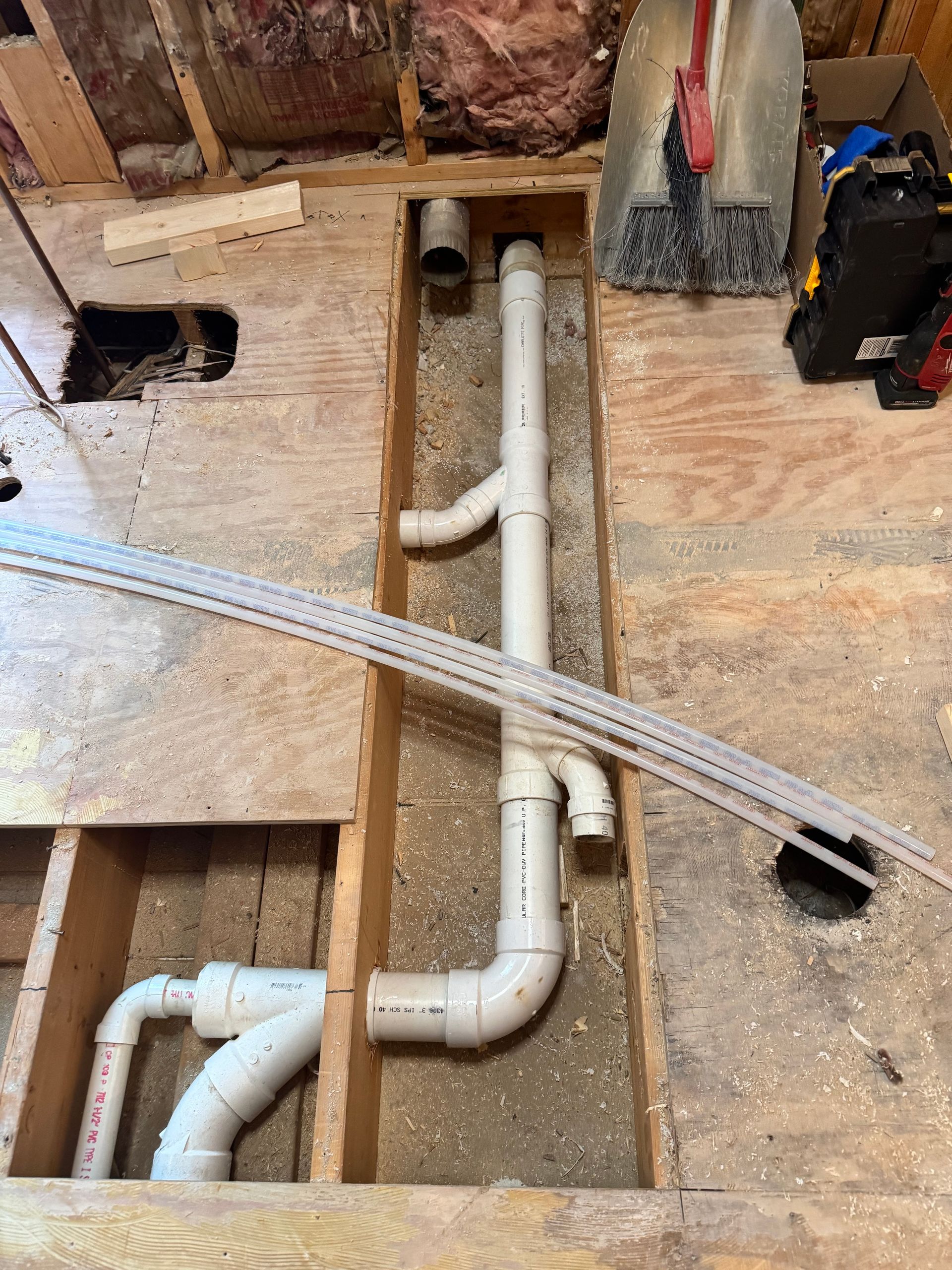 Plumbing pipes installed in a wooden floor opening during a home renovation.