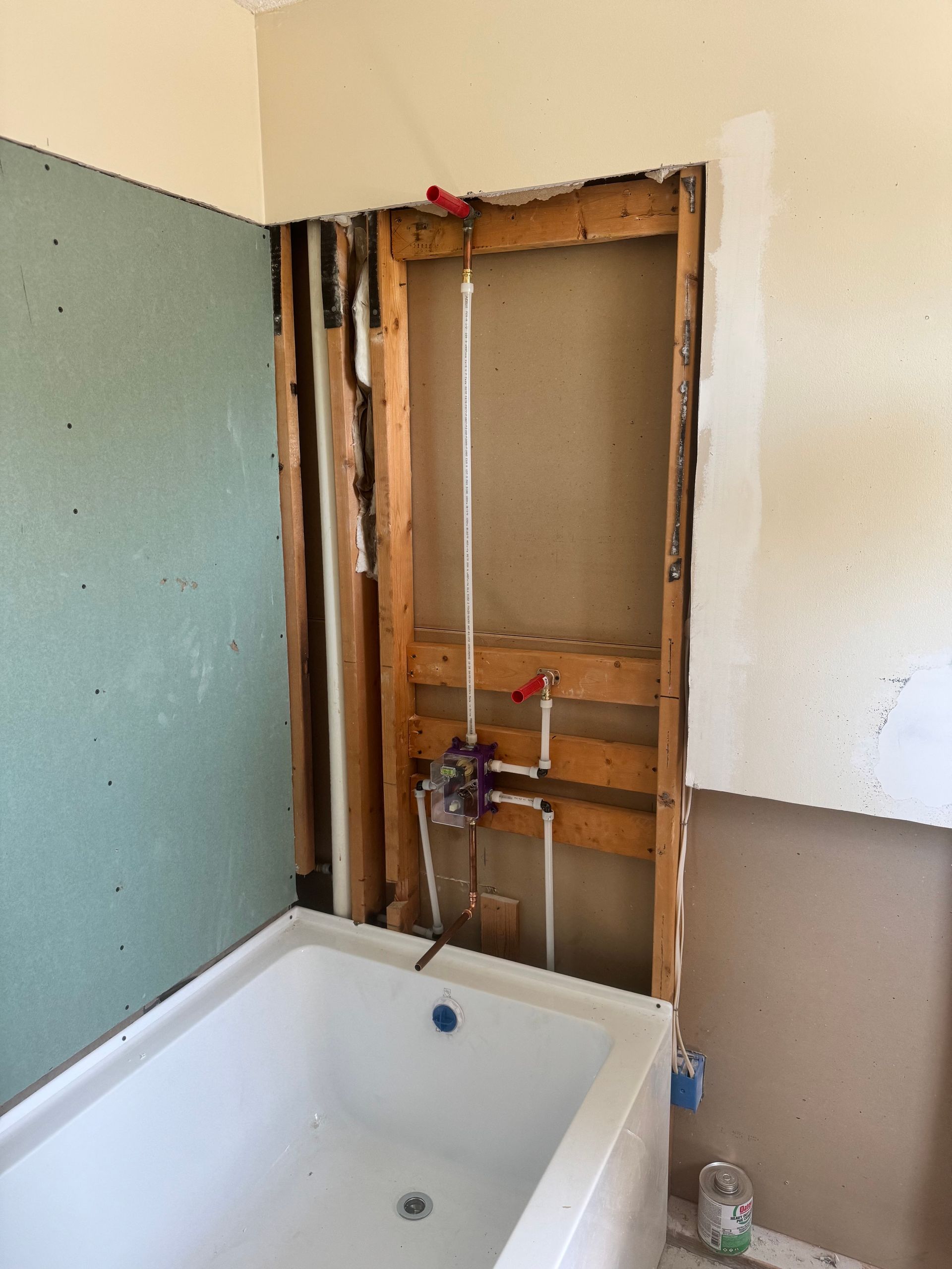 Bathroom renovation: tub, plumbing, exposed wall studs, drywall, pipes, and valve.