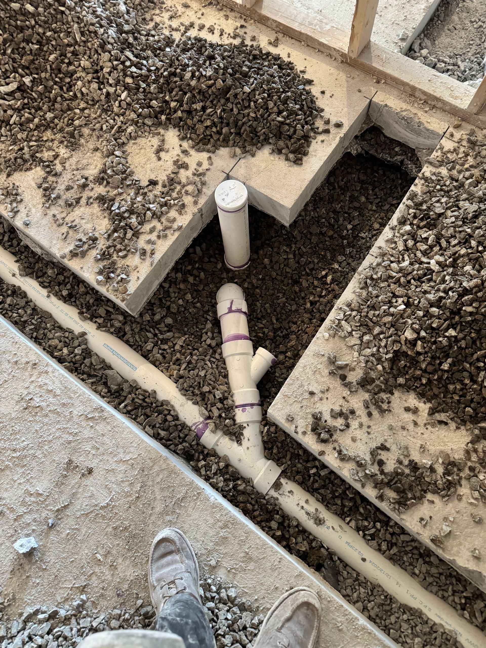 Plumbing pipes and gravel in an open concrete trench, likely during construction of a building.