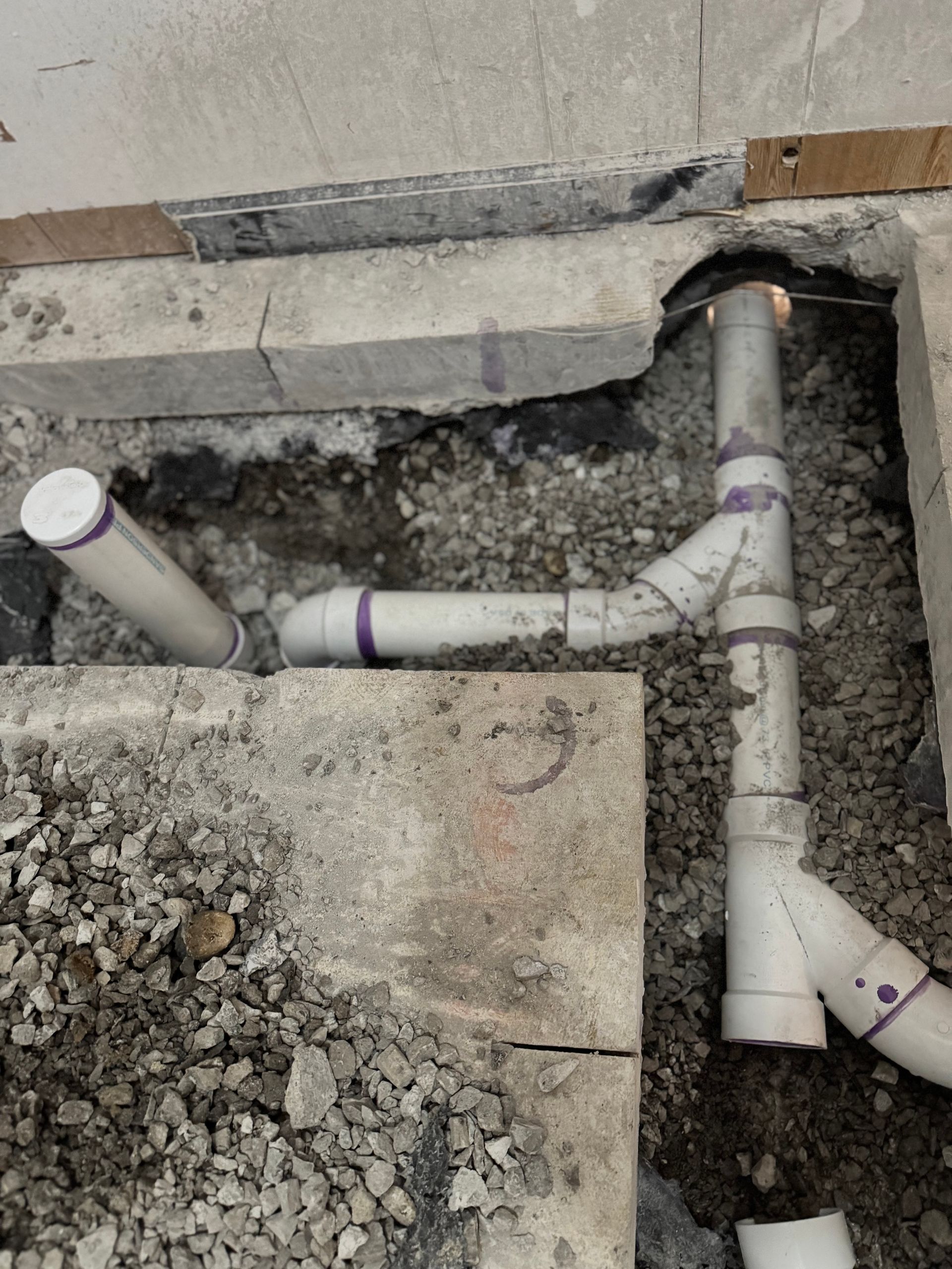 Pipes and fittings in a concrete floor trench, possibly for a bathroom, viewed from above.