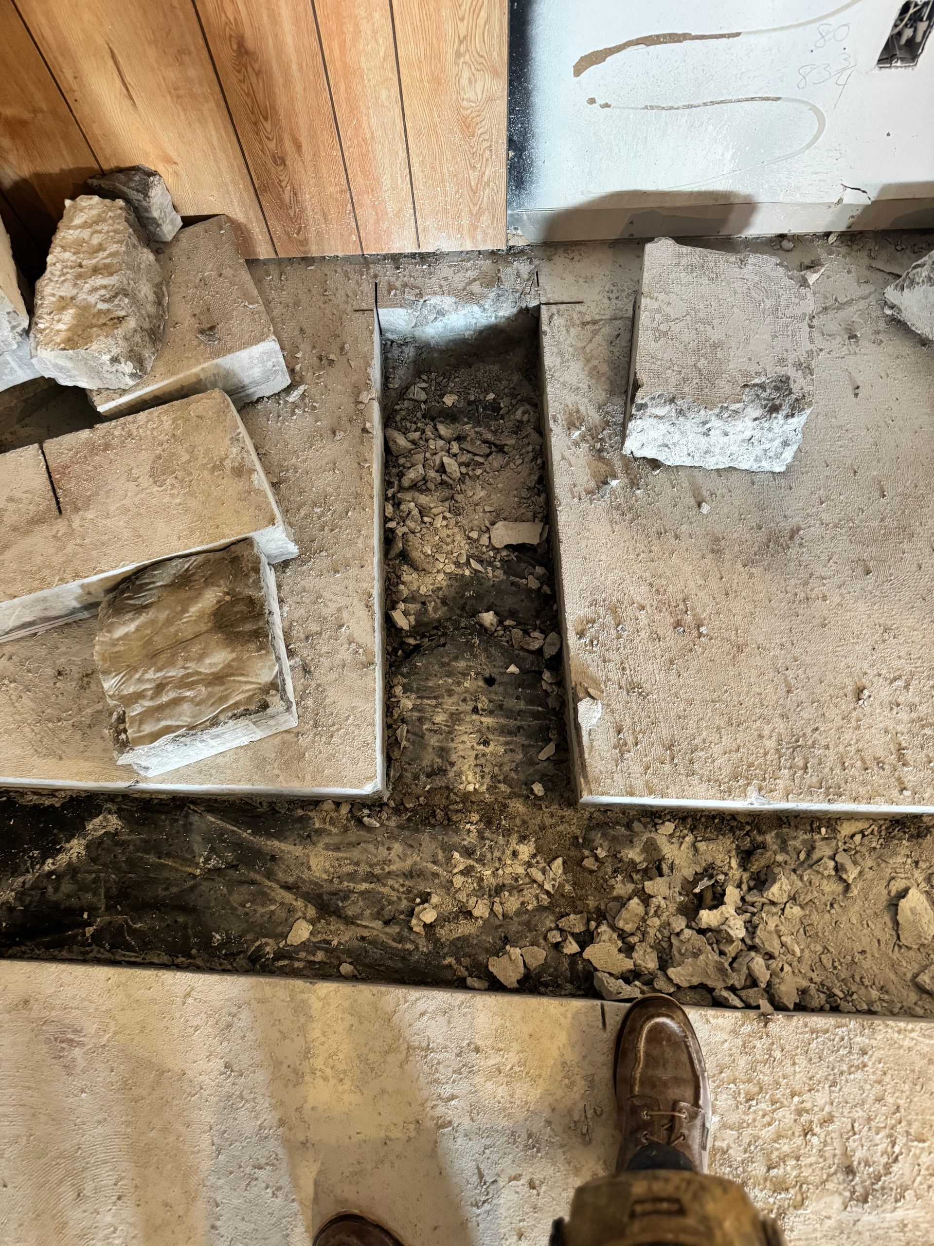 Tiles and subfloor removed, revealing a rectangular trench in a room.
