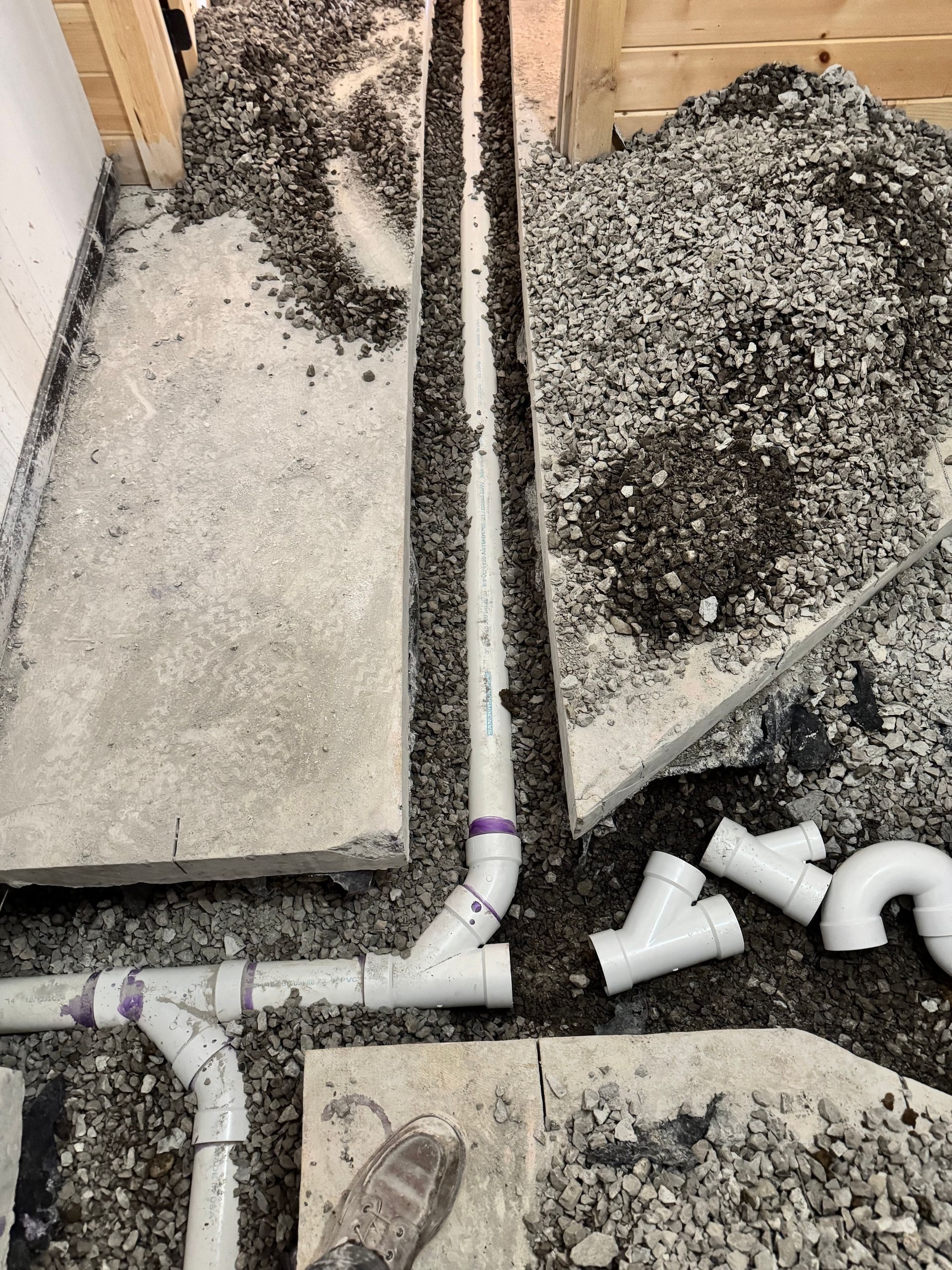 Pipes installed in a concrete floor trench, surrounded by gravel and debris. Plumbing work in progress.
