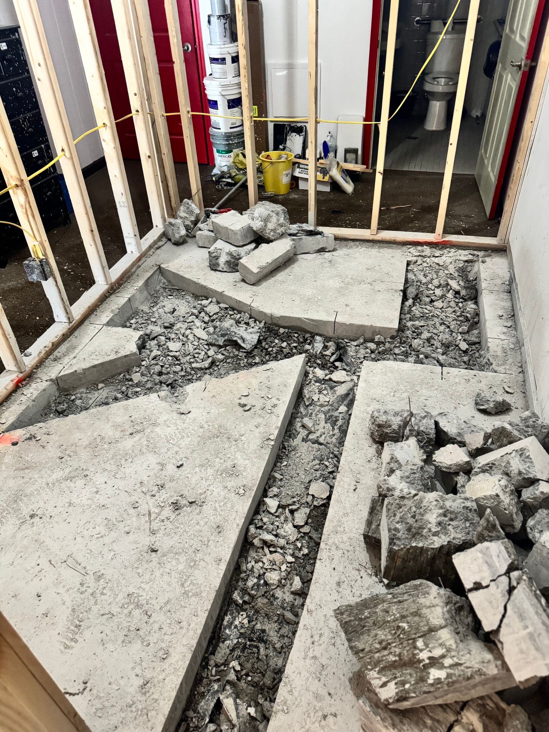 Construction site with concrete floor demolition. Debris and exposed trenches. Wood framing visible.