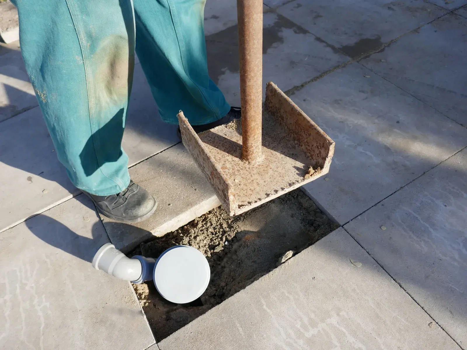 Person installing a drain on a patio, using a tool and filling the space with concrete.