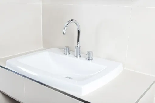White sink with chrome faucet and knobs in a beige bathroom.