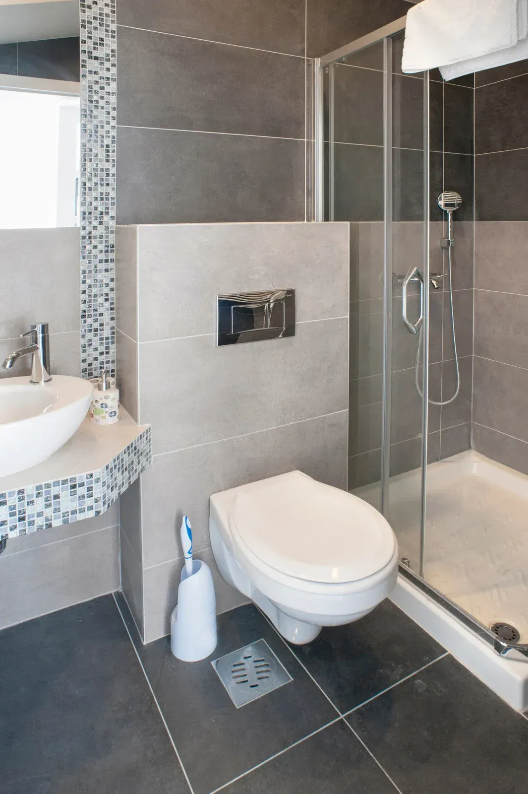 Modern bathroom with gray tile, a floating toilet, shower, and sink.