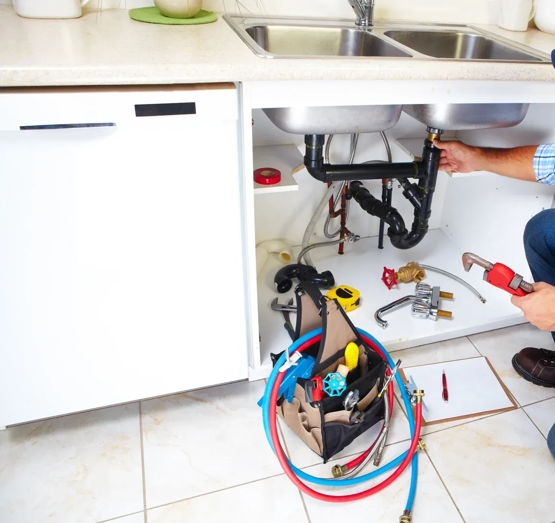 Plumber working under a kitchen sink with tools and pipes.
