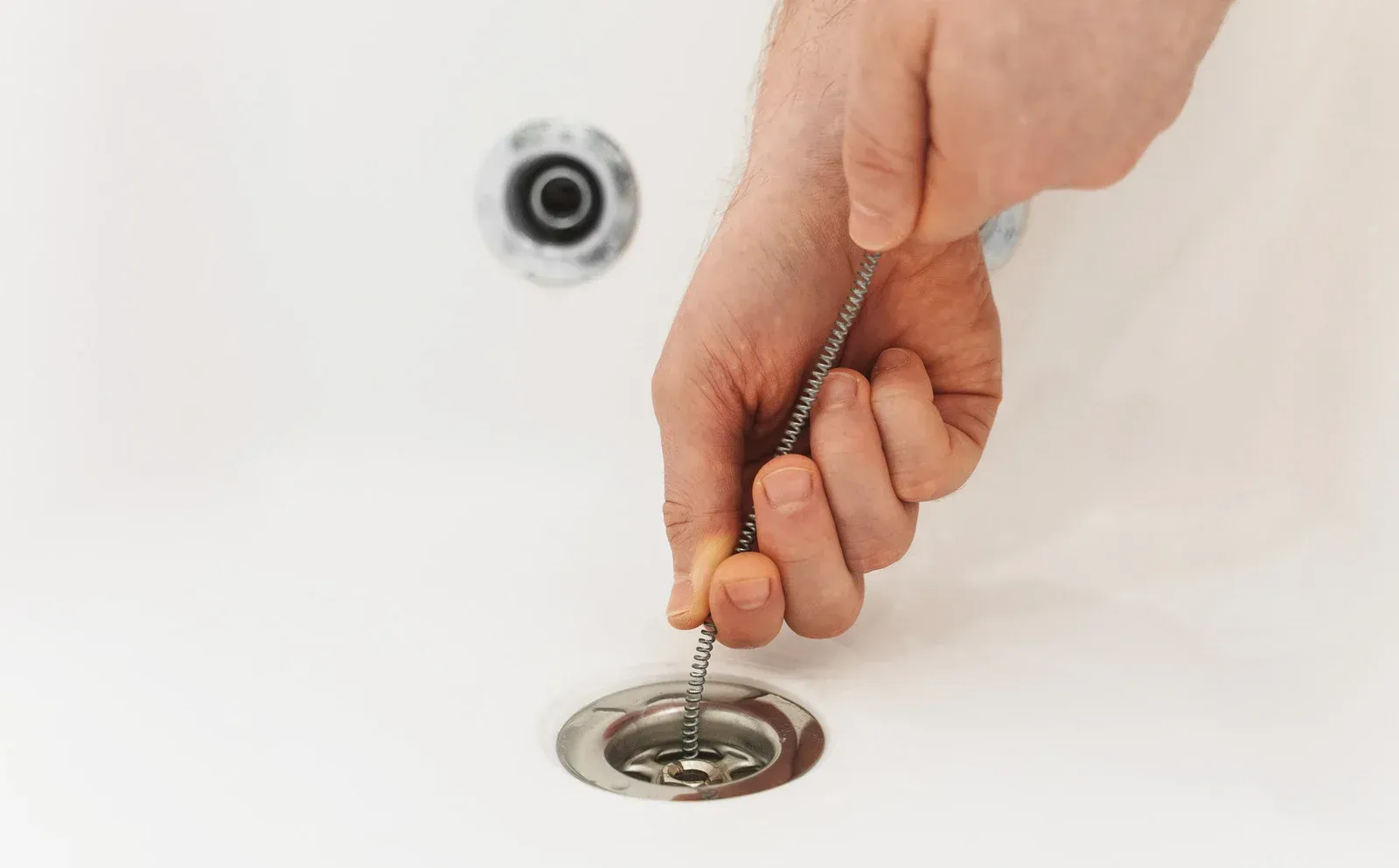 Hands pulling a drain plug chain in a white bathtub.