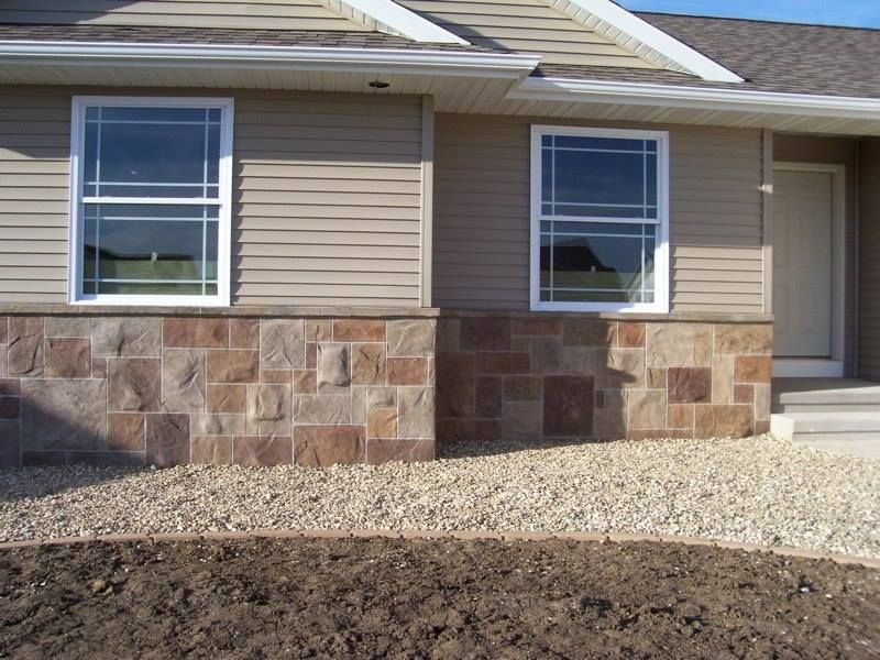 Tan house with stone base, two windows, and gravel landscaping.