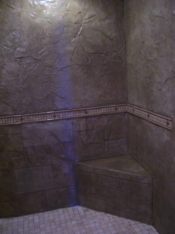 Brown stone-like shower interior with built-in corner seat, mosaic floor, and decorative tile trim.