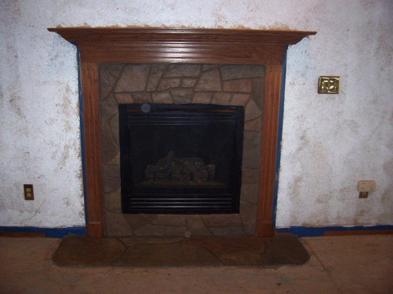 Fireplace with stone surround, wooden mantel, black interior, and tan hearth.