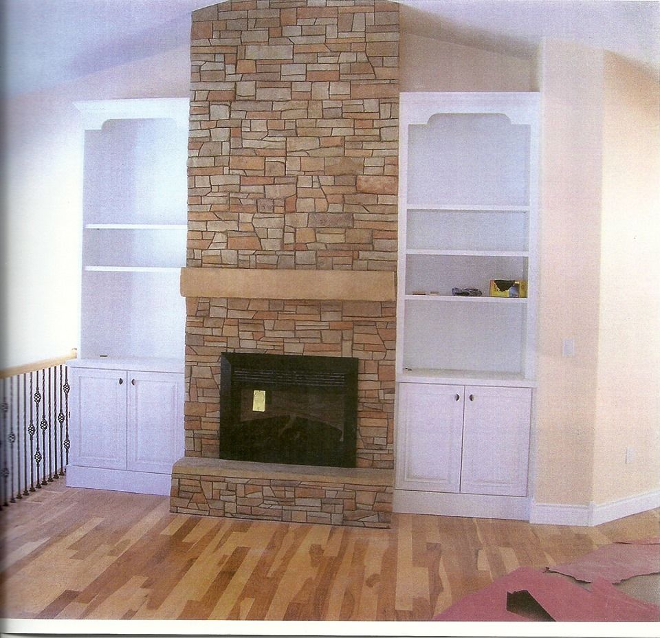 Fireplace with stone facade and white bookshelves on each side in a room with hardwood floors.
