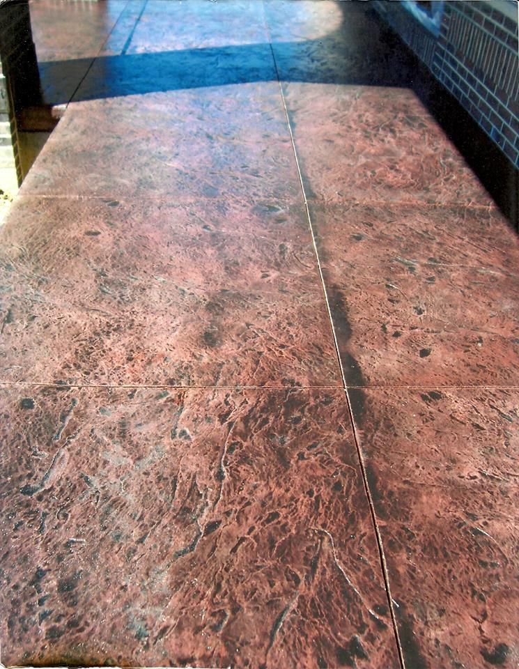 Textured reddish-brown concrete patio with a brick wall on the right side.