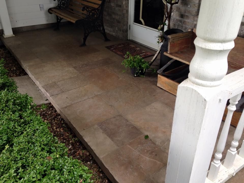 Stone porch with a bench, door, and bushes.