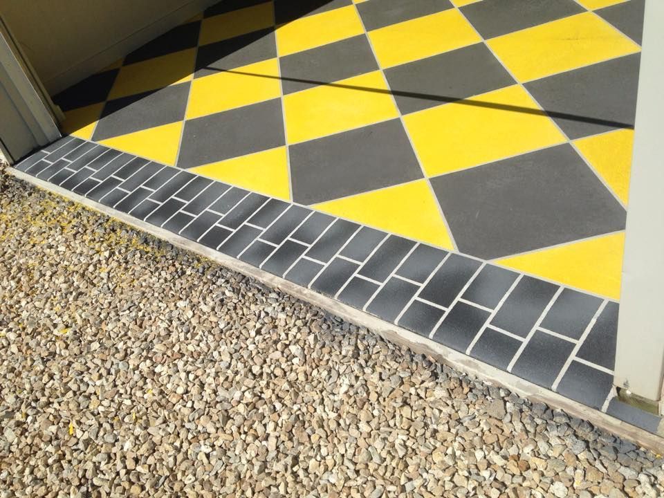Yellow and black checkered floor inside a garage, framed by a gray brick border and gravel.
