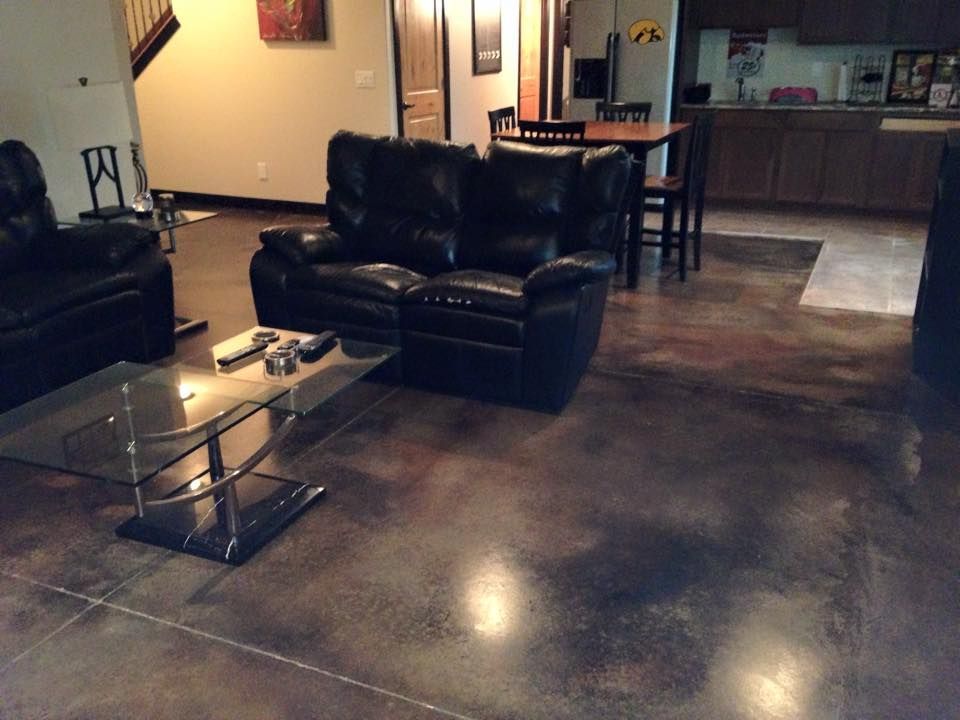 Living room with black leather furniture, glass coffee table, and stained concrete floor.