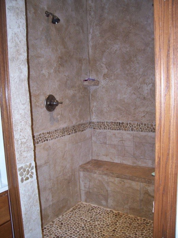 Shower with brown and beige stone tiles, including a bench and pebble floor.