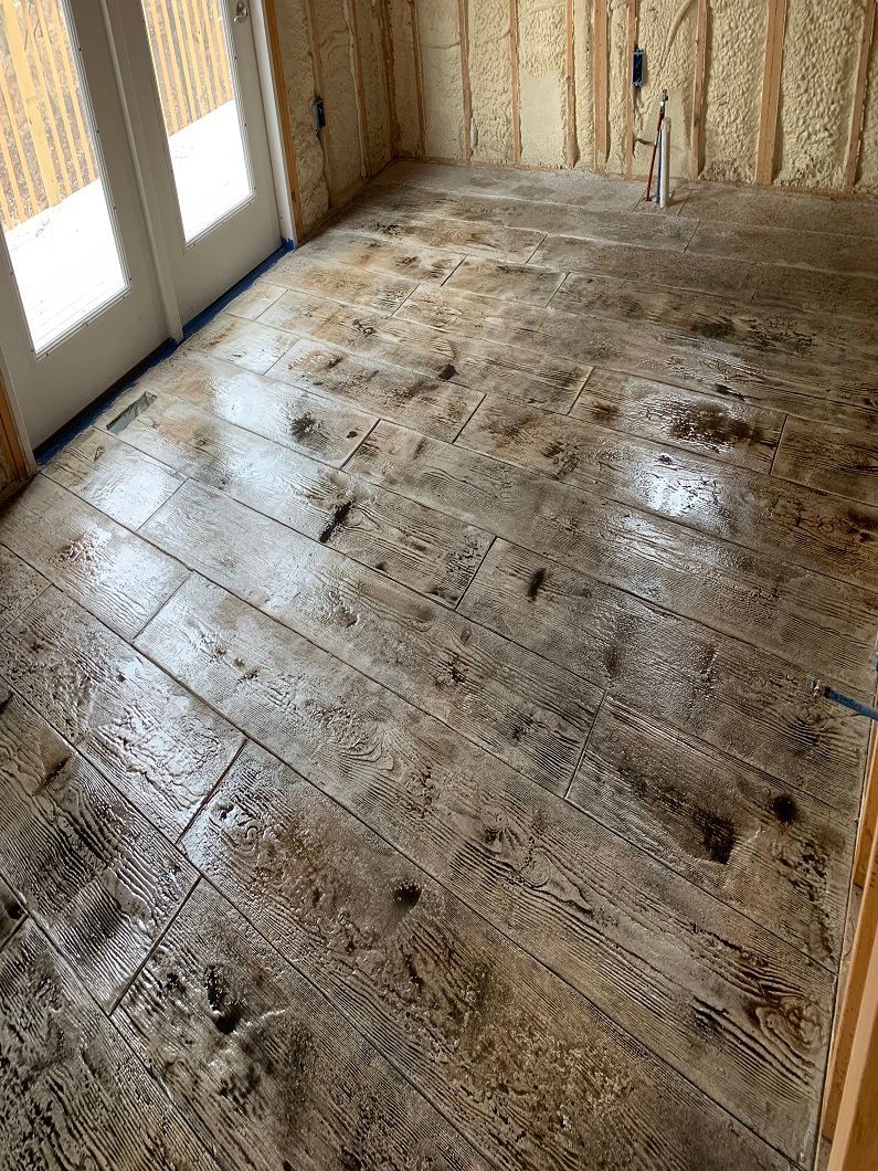 Concrete flooring with wood grain pattern, stained in shades of brown, installed inside a room.