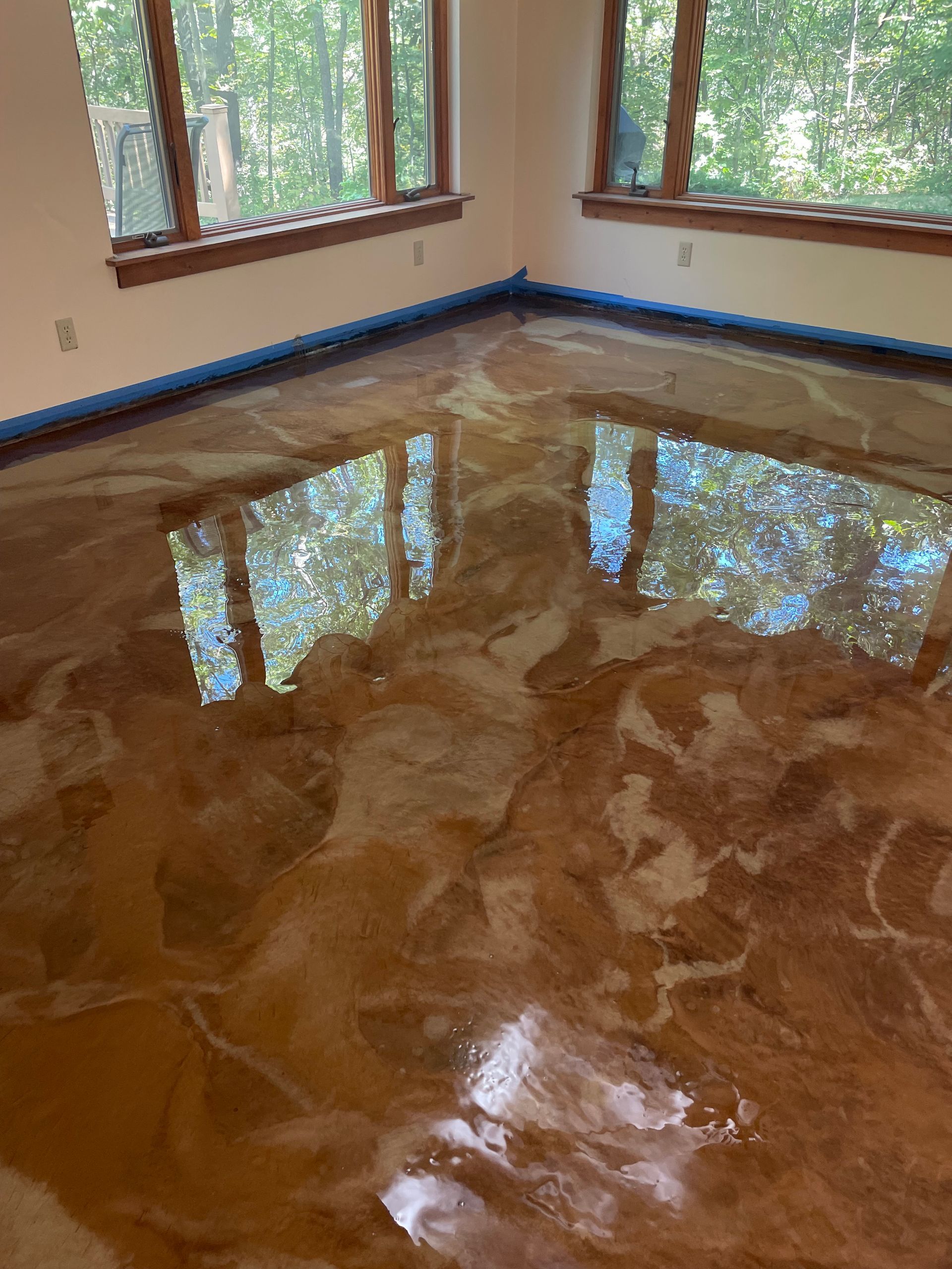 Metallic epoxy floor with brown and gold swirls, reflecting windows and sunlight.