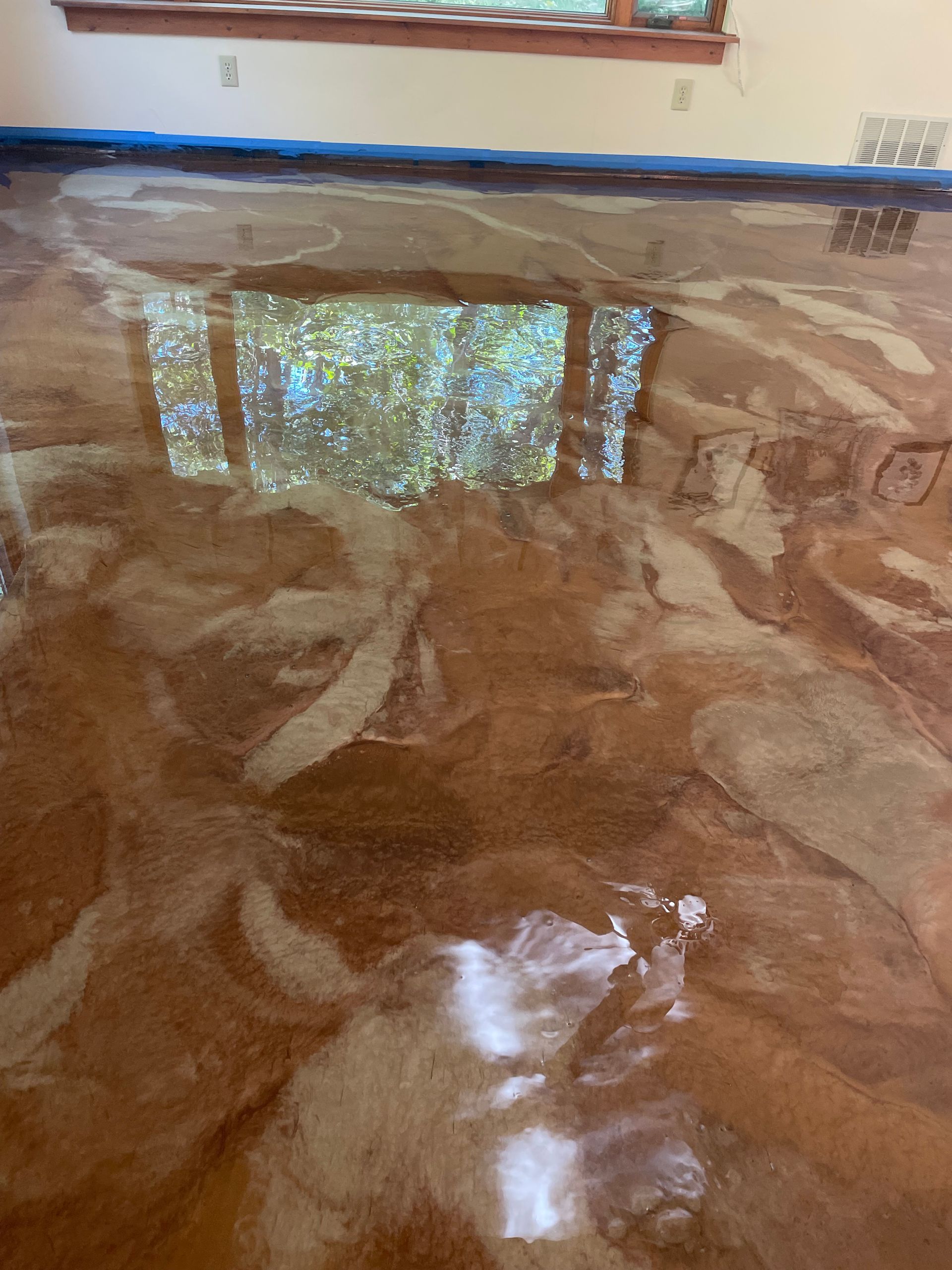 Metallic epoxy floor reflecting a window with greenery. The floor has brown and white swirling patterns.