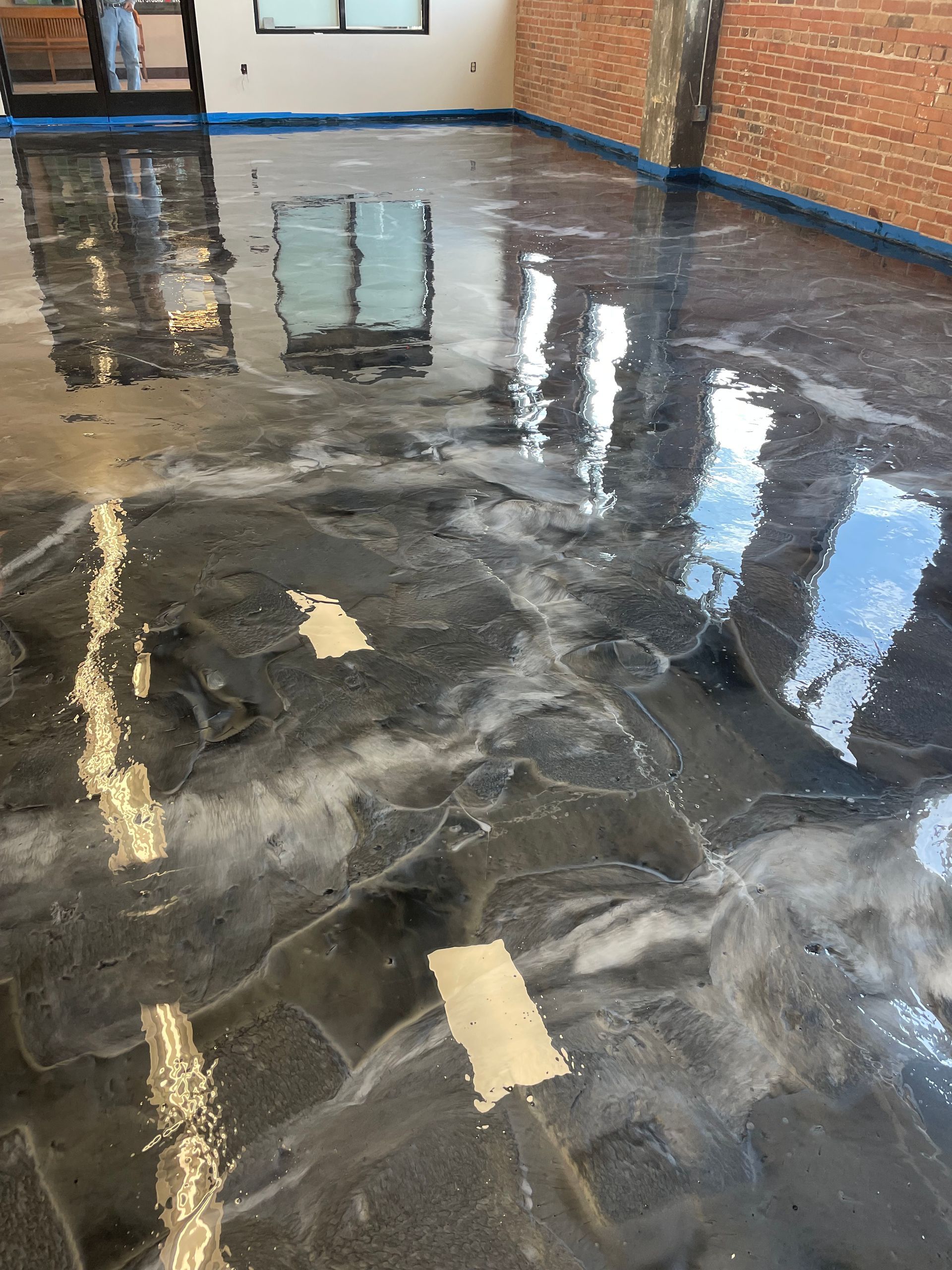 Shiny epoxy floor with swirls of black, silver, and white, reflecting light and windows.