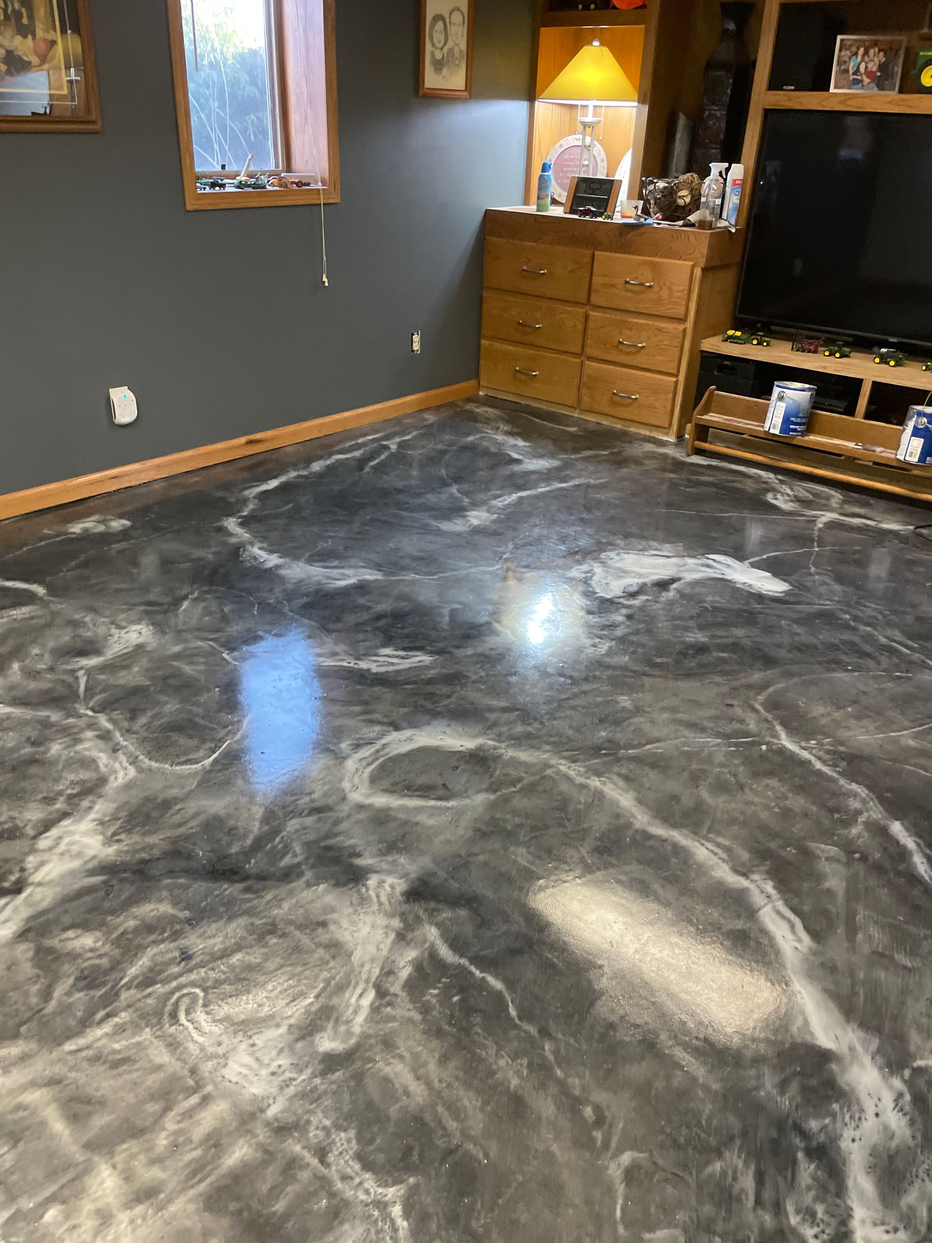 Metallic epoxy floor with marble-like swirls in gray and white, in a room with dark gray walls and wooden furniture.