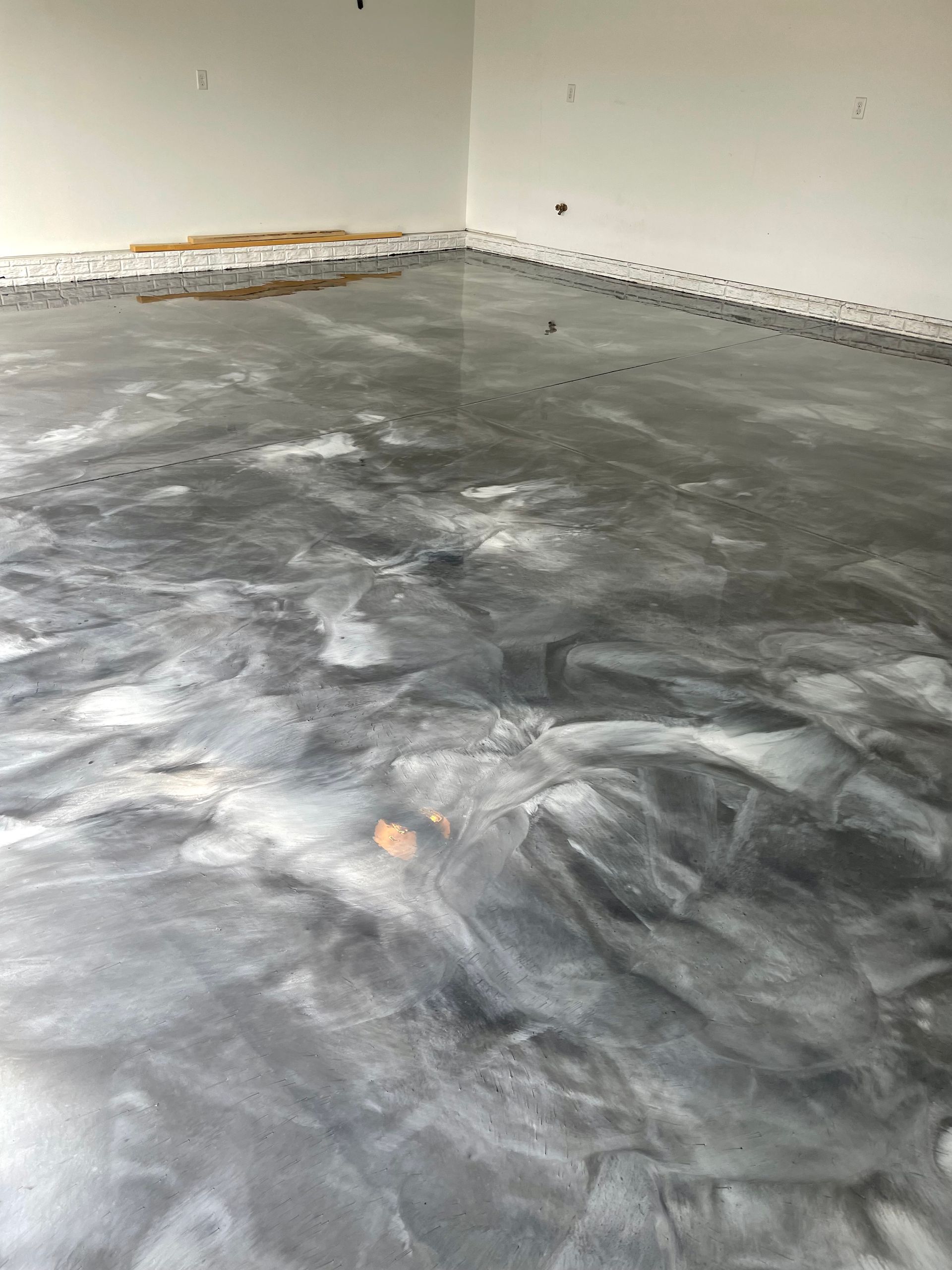Metallic epoxy floor in a room with white walls. Silver and dark gray swirls are visible.