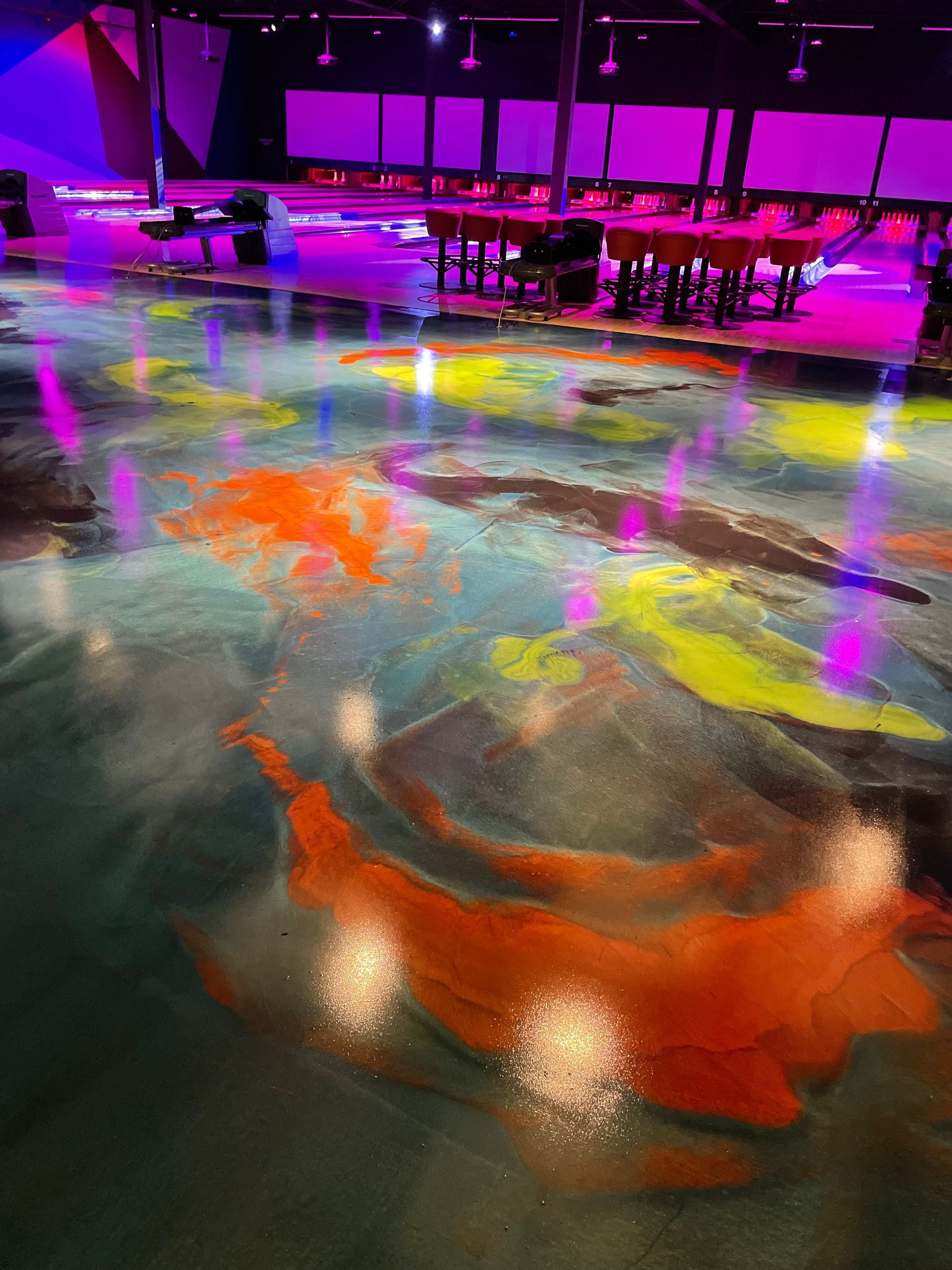Colorful epoxy floor with streaks of orange, blue, and yellow in an event space with purple lighting.