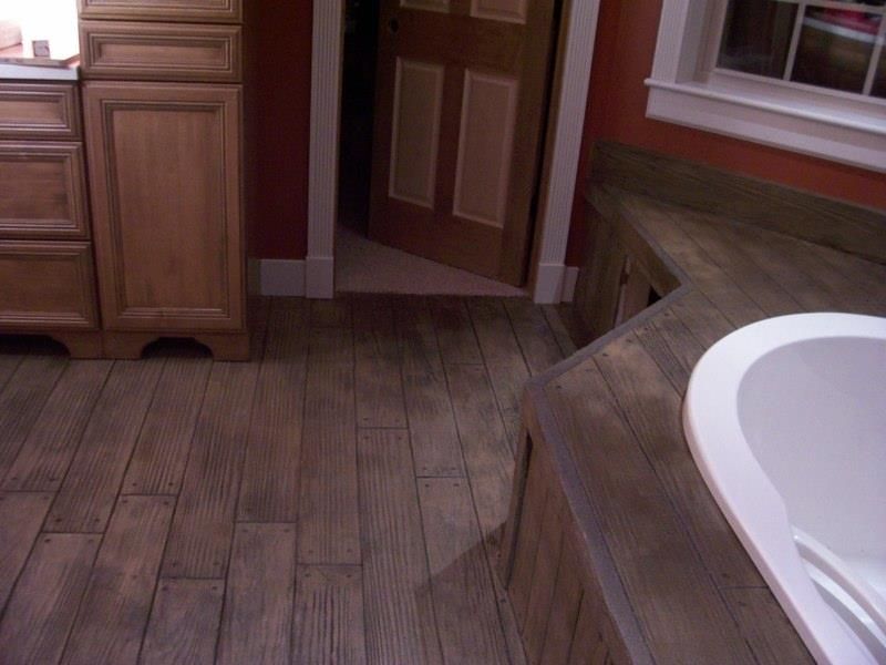 Bathroom with wood-look flooring, wooden cabinetry, and a white bathtub.