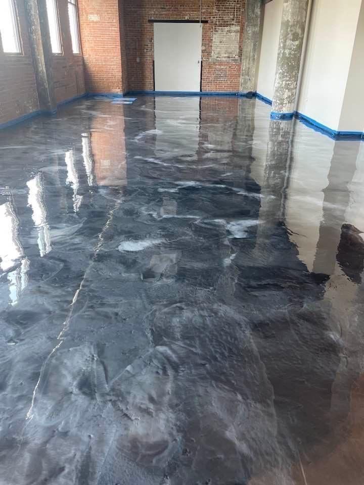 Glossy gray and white epoxy flooring in an industrial space with brick walls and a white screen.