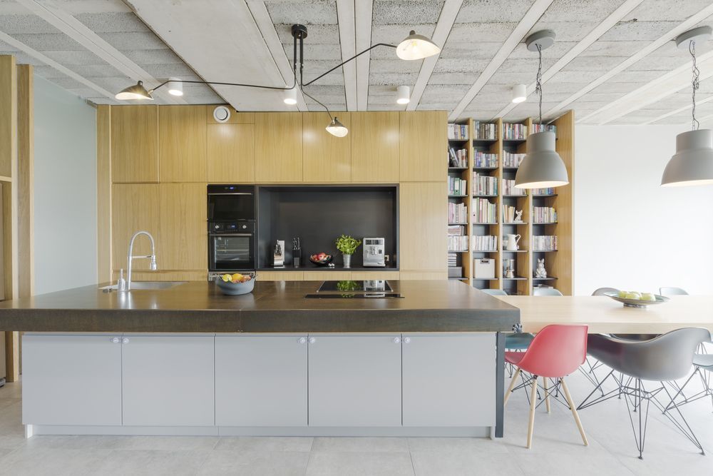 Modern kitchen with gray island, wood cabinets, open shelving, and dining area with colorful chairs.
