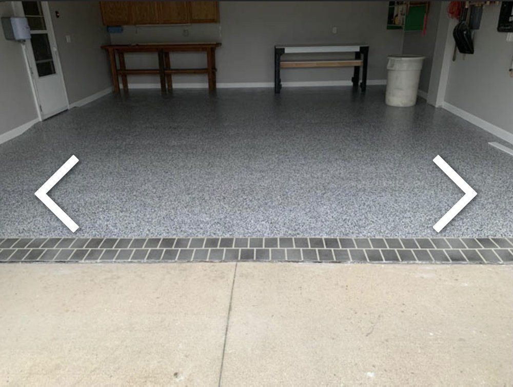 Garage with speckled epoxy floor and dark brick border, light concrete exterior.