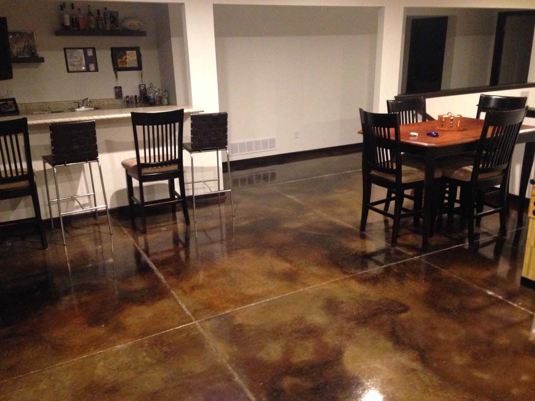 A room with a bar and dining table, featuring stained concrete floors. The room has dark wooden furniture.