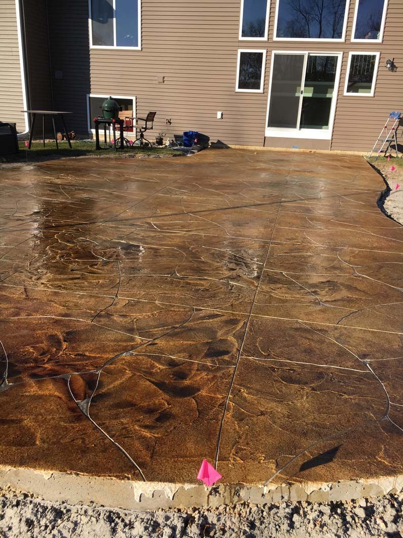 Large brown stamped concrete patio outside a house, with visible cracks and a pink marker.