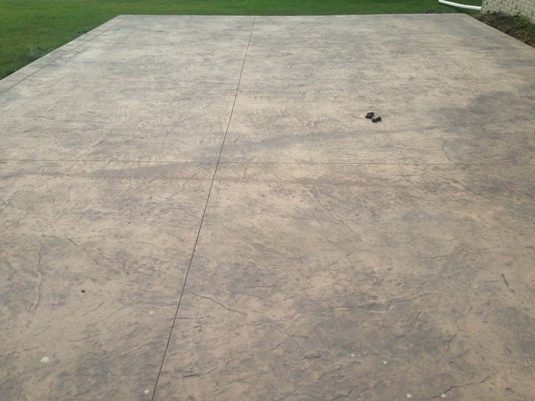 Gray concrete patio with two small, dark objects in the center and green grass in the background.