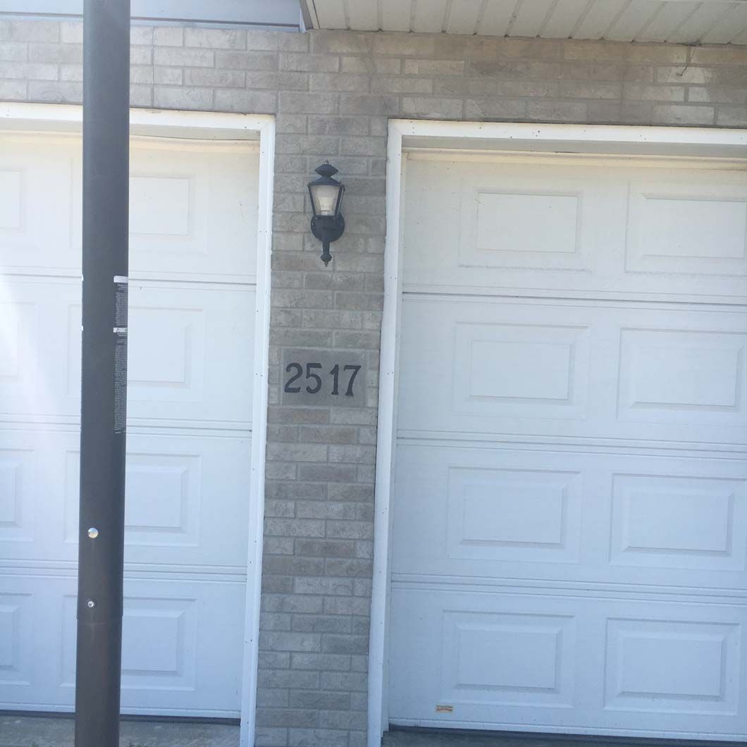 Two white garage doors with the address 2517 on the brick wall in between. A black lamp is above the number.