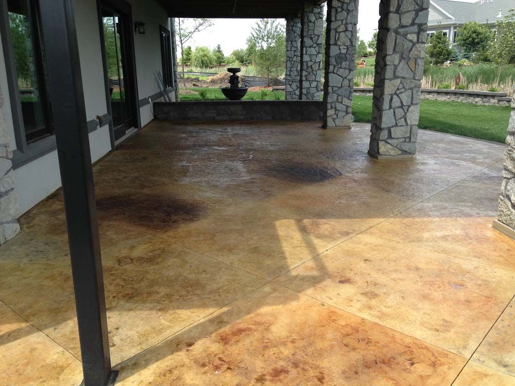 Patio with stained concrete floor, stone columns, and view of a fountain and yard.