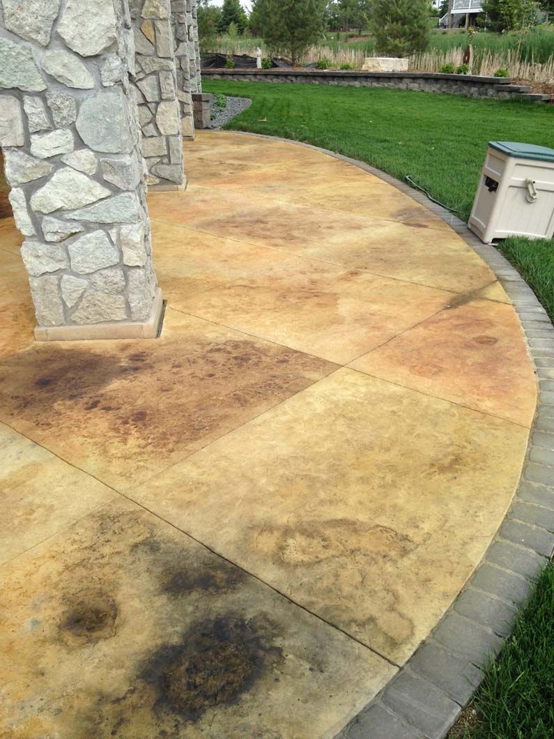 Stone column supports a concrete patio with stained patterns, bordered by a brick edge and grass.